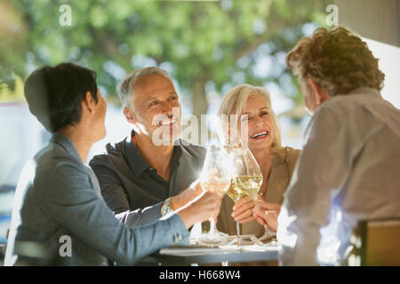 Couples toasting white wine glasses at sunny restaurant table Stock Photo