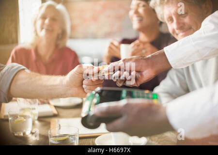 Man paying waiter with credit card machine at restaurant table Stock Photo