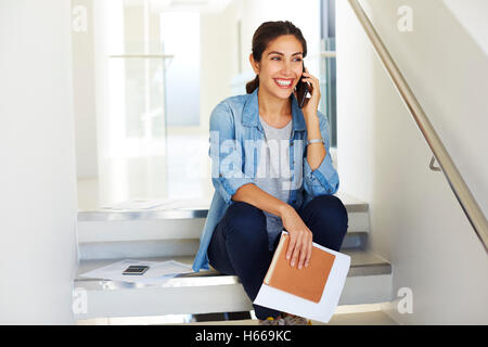 Smiling businesswoman with paperwork talking on cell phone in stairway Stock Photo