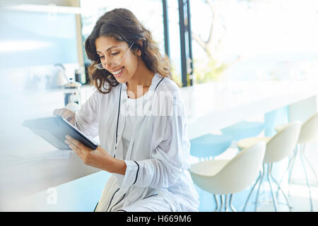 Smiling businesswoman in bathrobe working using digital tablet in kitchen Stock Photo