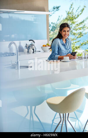 Portrait smiling woman using cell phone at kitchen counter Stock Photo