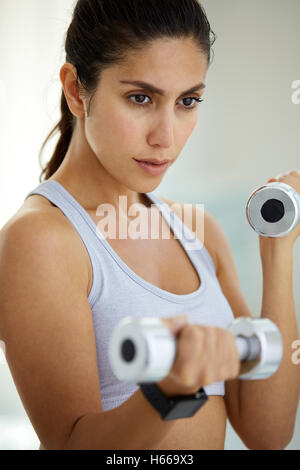 Determined brunette woman doing biceps curls with dumbbells Stock Photo