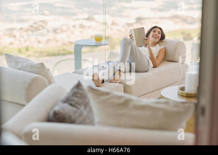 Smiling woman reading book relaxing on chaise lounge Stock Photo