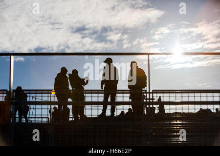 Toursits visting the rift valley in the Pingvellir national Park home of the ancient Icelandic parliement in Iceland, walk silhouetted against thje sun on top of the cliff. Stock Photo
