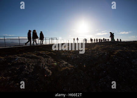 Toursits visting the rift valley in the Pingvellir national Park home of the ancient Icelandic parliement in Iceland, walk silhouetted against thje sun on top of the cliff. Stock Photo