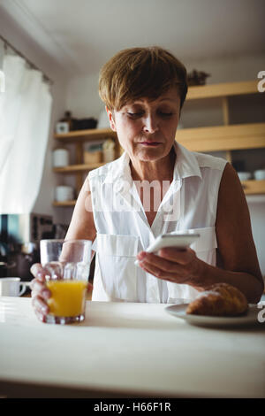 Senior woman using mobile phone while having breakfast Stock Photo
