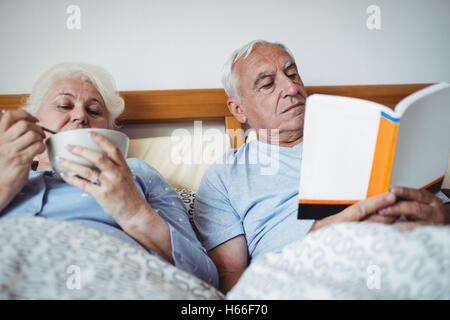 Senior man reading novel and woman having breakfast Stock Photo