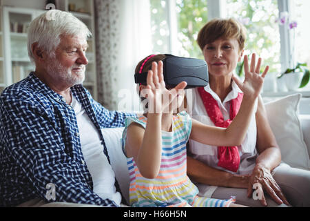 Granddaughter using virtual reality headset with her grandparents in living room Stock Photo