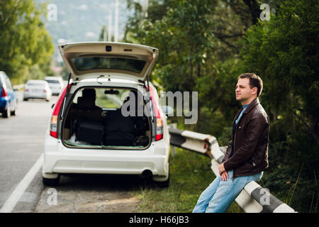 Road trip break after long drive. Man waiting for someone sitting on the fence. Stock Photo