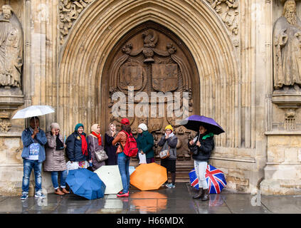 Asian tourists sheltering from rain in Bath. Visitors to UNESCO World Heritage City of Bath hide in the doorway of Bath Abbey Stock Photo