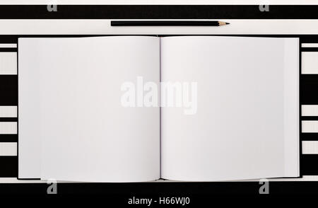 high-angle shot of a black pen and an open notepad with blank pages on a black and white surface Stock Photo