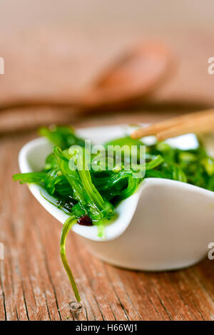 goma wakame or seaweed salad in a white ceramic bowl, on a rustic wooden table Stock Photo