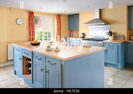 A large country kitchen with traditionally styled units in blue with solid wood work surfaces, yellow walls & a range cooker Stock Photo