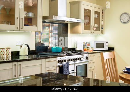 A contemporary open plan kitchen incorporating a range cooker, hood & granite work surfaces. Oxfordshire, UK Stock Photo