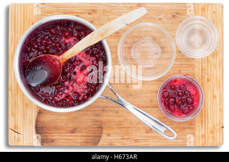 Top down view on cranberry sauce in stainless steel metal saucepan beside three different sized bowls over cutting board Stock Photo