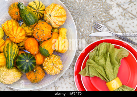 Colorful Thanksgiving centerpiece with ornamental gourds in different colors of orange and green alongside a matching place sett Stock Photo