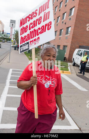 Mature ethnic woman nurse carrying placard protesting new health benefits package at Allina Health Minneapolis Minnesota MN USA Stock Photo