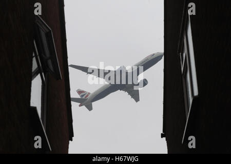 A British Airways plane flies past an alleyway between two houses in Longford Village, Hillingdon, near Heathrow Airport, as the long-awaited decision on which airport expansion scheme should get the go-ahead is to be finally made. Stock Photo