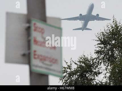 An American Airlines plane flies past a Stop Heathrow Expansion protest sign in Longford Village, Hillingdon, near Heathrow Airport, as the long-awaited decision on which airport expansion scheme should get the go-ahead is to be finally made. Stock Photo
