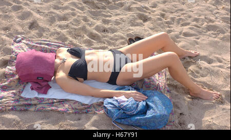A woman in her mid-forties sunbathes whilst lying covering her face with clothing Stock Photo