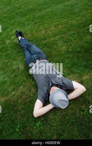 businessman lying in a field on green grass with the hat over his face. Passive income Stock Photo