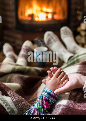 Warming and relaxing near fireplace. Mother and daughter holding hands in front of fire. Stock Photo