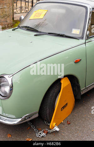 Nissan Figaro classic car with yellow triangle wheel parking clamp attached. In Nottingham Stock Photo