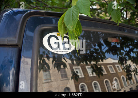 GB 'AA' car sticker back window of Land rover discovery, street reflected with leaves hanging over the window and sign Stock Photo