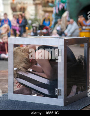 Circus contortionists squeeze into a small glass Cube at Southport. A contortionist woman enters & exits (Enterology) into a small, knee-high cube box. Performing flexible female contortionists show an insane stretching routine as the cabaret show entertains the audience at Pleasureland,  Merseyside UK. Stock Photo