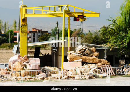 Yellow crane used for lifting stone slabs and blocks at a stonemason's yard. Stock Photo