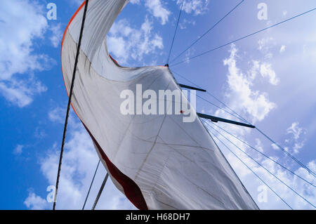 White canvas sails of a sailing ship against a blue sky with some clouds. Stock Photo