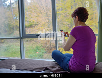 Woman using her smartphone on bed at hotel room Stock Photo
