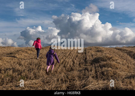 Two children running up hill in a stubble field Stock Photo