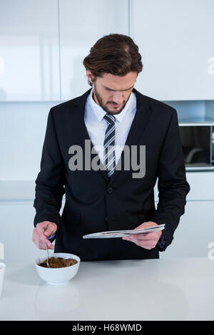 Businessman reading newspaper while having breakfast in kitchen Stock Photo