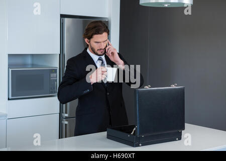 Businessman talking on mobile phone in kitchen Stock Photo