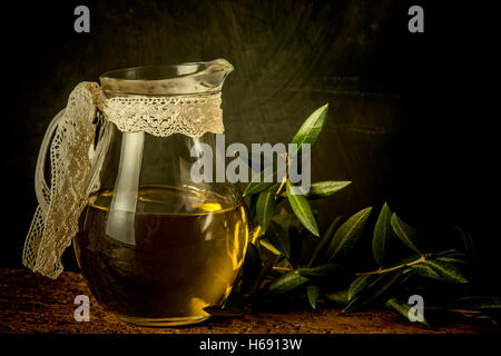 Extra virgin olive oil glass jar and leaves on rustic background Stock Photo