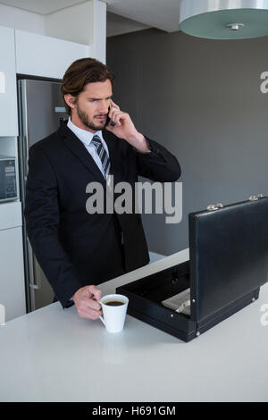 Businessman talking on mobile phone in kitchen Stock Photo