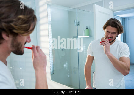 Man looking in mirror while brushing her teeth in bathroom Stock Photo