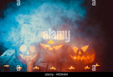 Three glowing pumpkins symbolizing the head of old Jack, with smoke on wooden background. Soft focus. shallow DOF Stock Photo