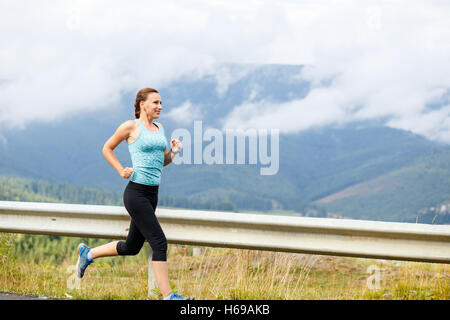 Young athletic woman jogging on road in mountains after rain Stock Photo