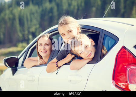 Happy young woman and her children sitting in a car and look out from windows. Family travel warm color toned image Stock Photo