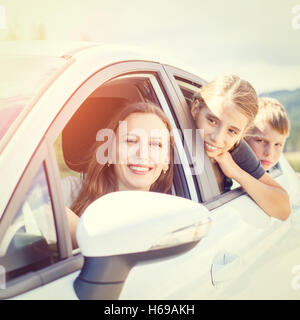 Happy young woman and her children sitting in a car and look out from windows. Family travel warm color toned image Stock Photo