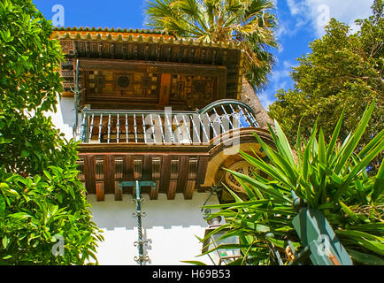 The medieval wooden balcony with forged metal railings and hand painted sailing, surrounded by green trees and bushes, Seville Stock Photo