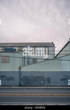 Old warehouse painted blue and grey with cleaned graffiti and nice doors and covered windows on a flat, cloudy day Stock Photo