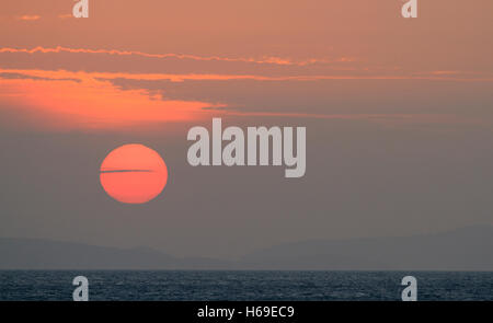 Sunset over the ocean with clouds in front of a big red disc sun. Stock Photo