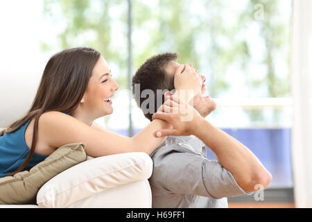 Playful couple covering eyes at home with a window in the background Stock Photo
