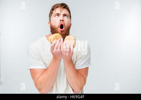 Excited bearded man enjoying eating hamburgers isolated on white background Stock Photo