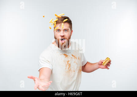 Funny bearded man in dirty shirt throwing french fries isolated on white background Stock Photo