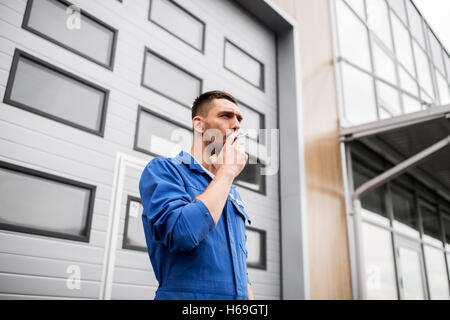 auto mechanic smoking cigarette at car workshop Stock Photo