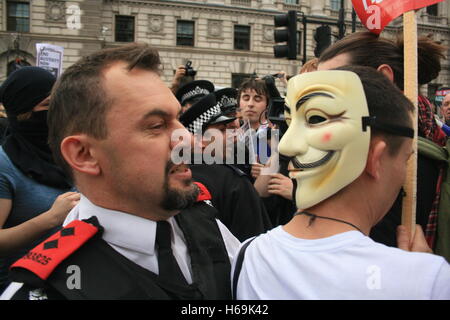 Police Inspector 193825 pulls and pushes the back of a protester wearing an anonymous mask, who has his back turned to him during a protest against the re-election of the Conservative Party in Whitehall. Demonstrators clash with police. Stock Photo